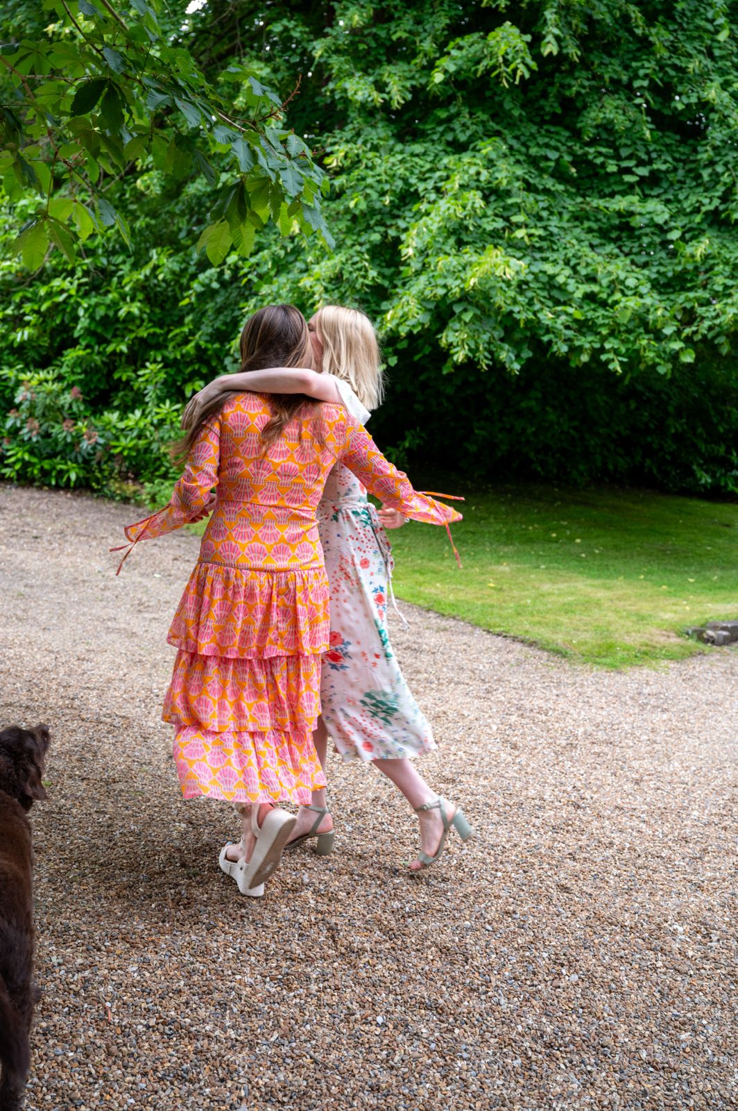 Two guests in bright summer dresses embracing on a gravel driveway