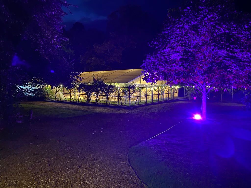 Illuminated marquee at dusk surrounded by trees lit in purple