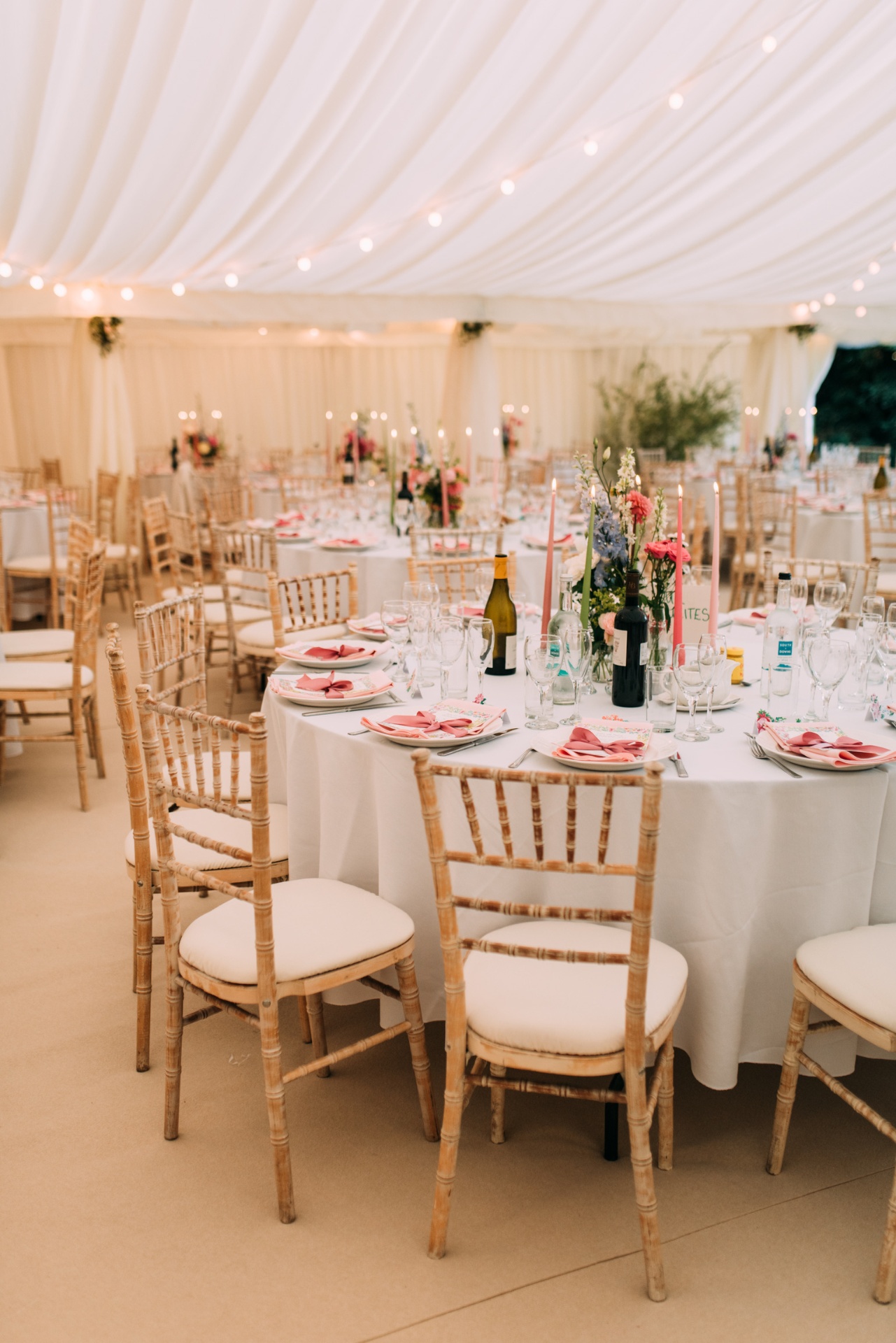 Elegant wedding marquee with round tables, chiavari chairs, floral centrepieces and soft draped ceiling lighting