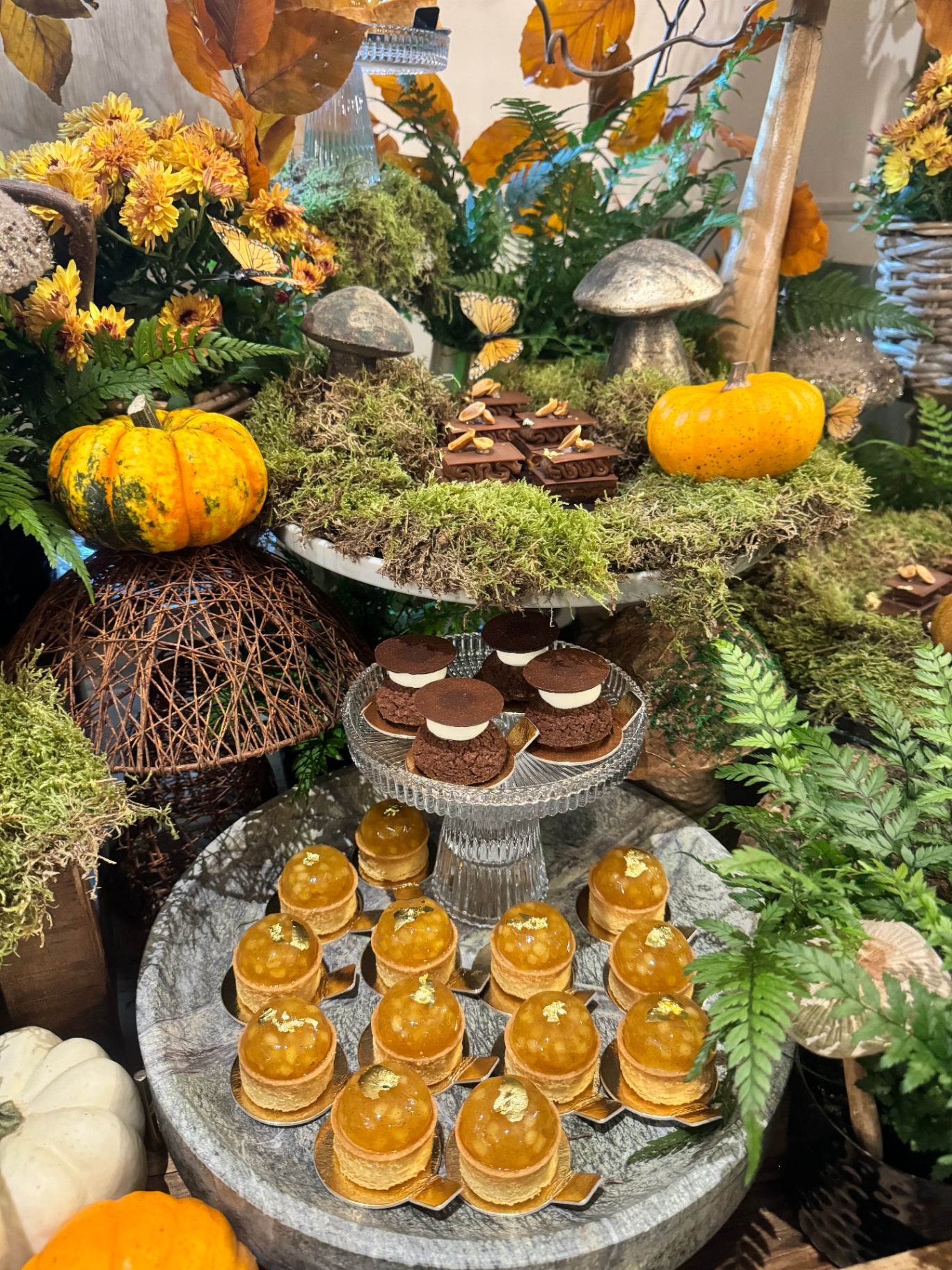 Autumn-themed dessert display with pumpkins, moss, ferns and pastries