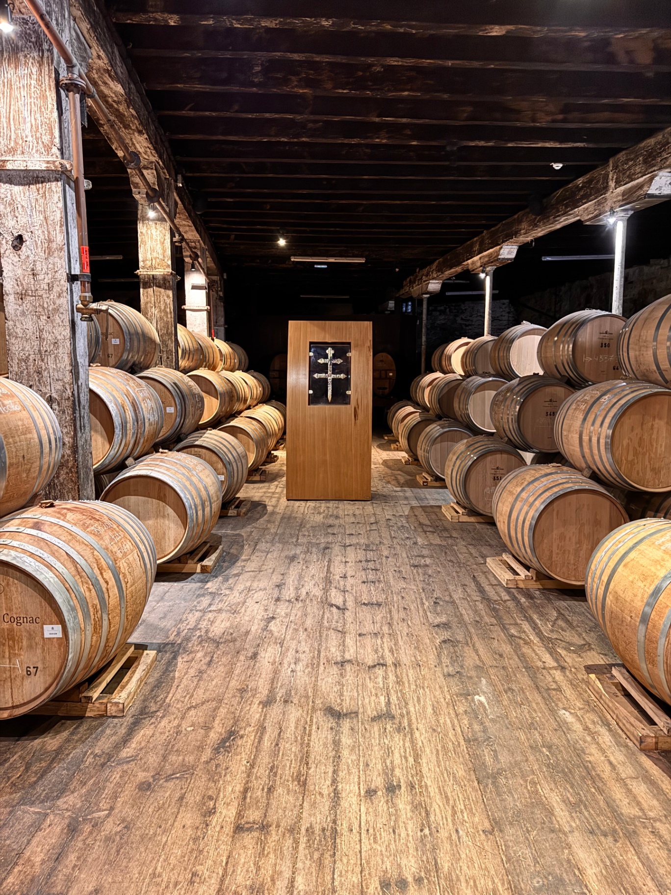 Cognac cellar with oak barrels stacked along timber-beamed aisle